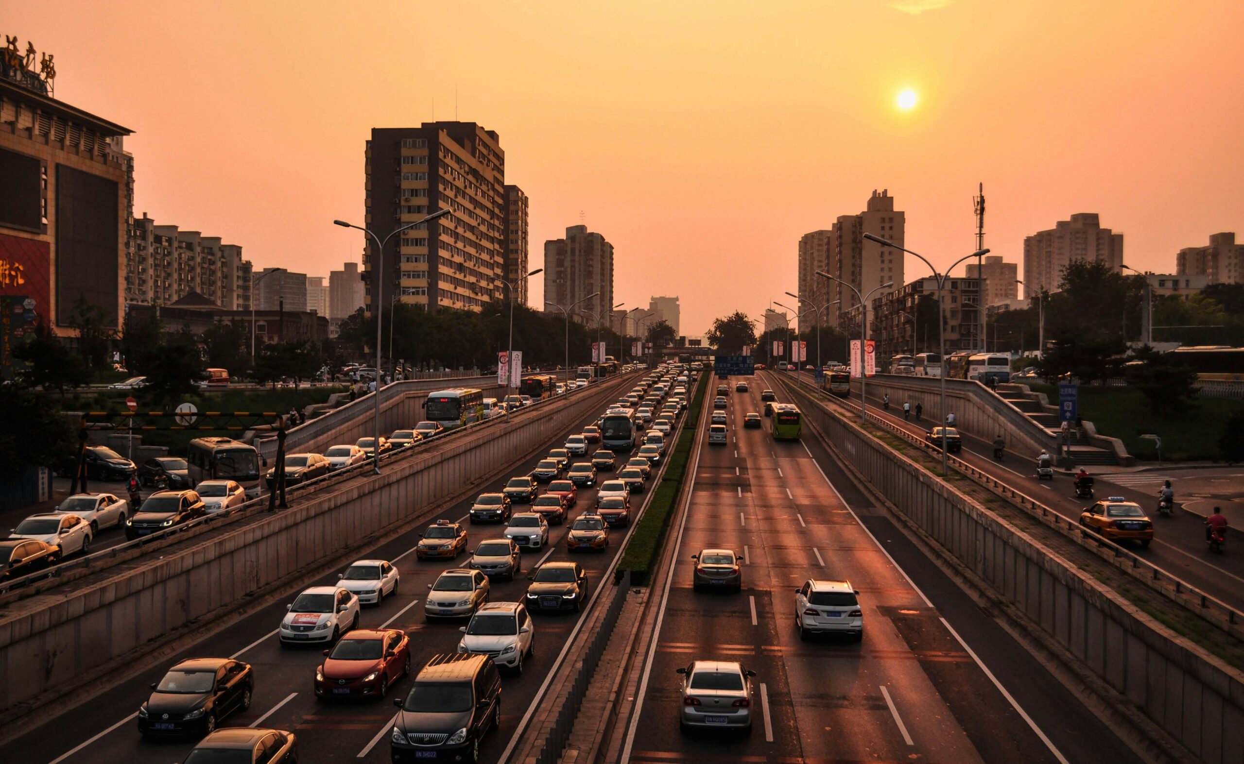 A bustling urban highway with heavy traffic under a vibrant sunset sky against a cityscape backdrop.